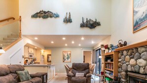 A spacious living area with a fireplace, a stone wall, and a kitchen in the background. - Cozy three-bedroom condo w summer pool (FP1-15) (Incline Village)