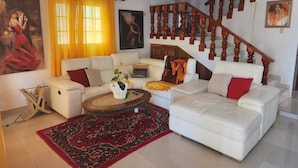 Un salon avec un ensemble de canapés blancs, une table basse, un tapis à motifs rouges et un escalier avec des rampes en bois.