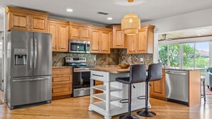 Une cuisine moderne avec des meubles en bois, des appareils en acier inoxydable, un plan de travail en granit et un coin bar avec des tabourets.