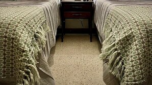 Quarto de hotel com duas camas, uma mesa de cabeceira, abajur e arte decorativa na parede.