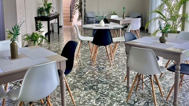 Um quarto espaçoso com piso estampado, várias mesas e cadeiras, e plantas em vasos.