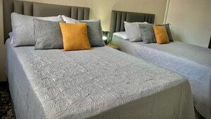 Quarto de hotel com duas camas, cada uma com colcha cinza e várias almofadas.