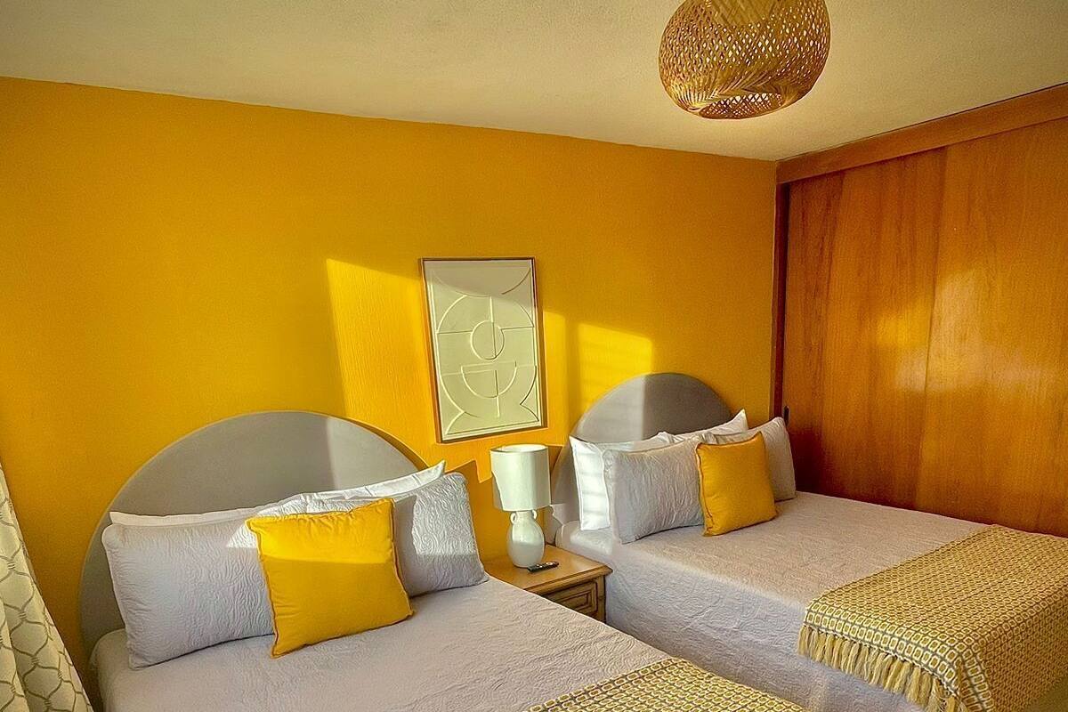 Ein Hotelzimmer mit zwei Betten, einem Holzschrank, einem Nachttisch mit Lampe und einem an der Wand hängenden Kunstwerk.
