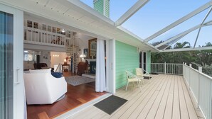 Una amplia terraza con piso de madera, barandal blanco y pared exterior verde.