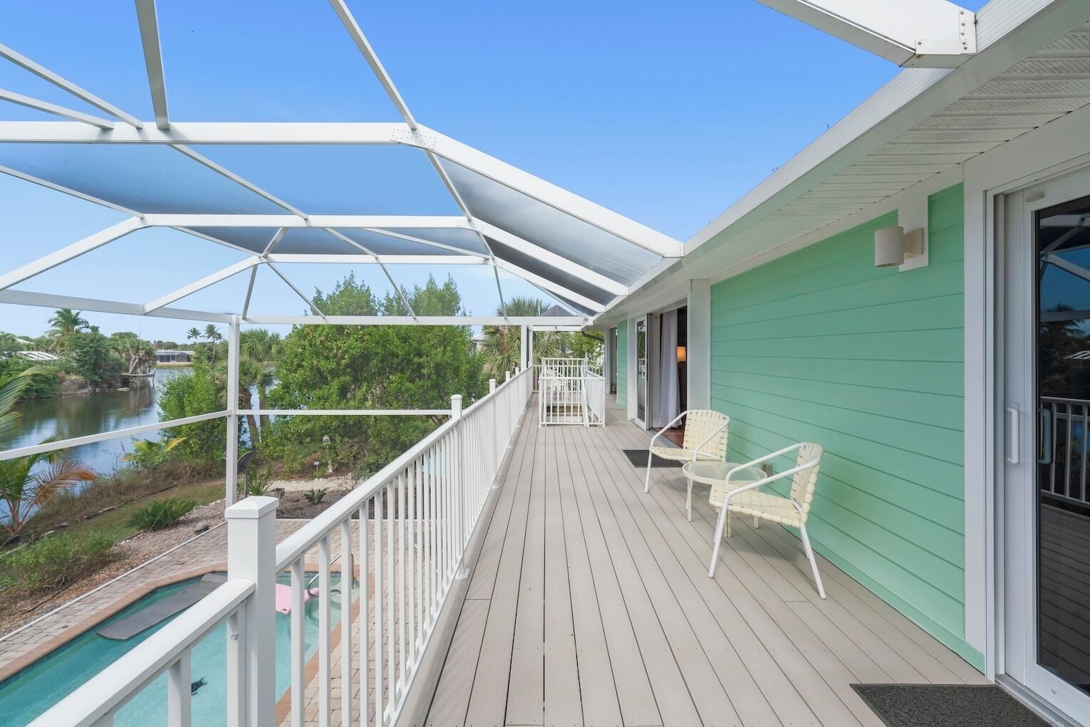 A covered deck with a pool, chairs, and a view of a river.