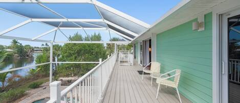 A covered deck with a pool, chairs, and a view of a river.