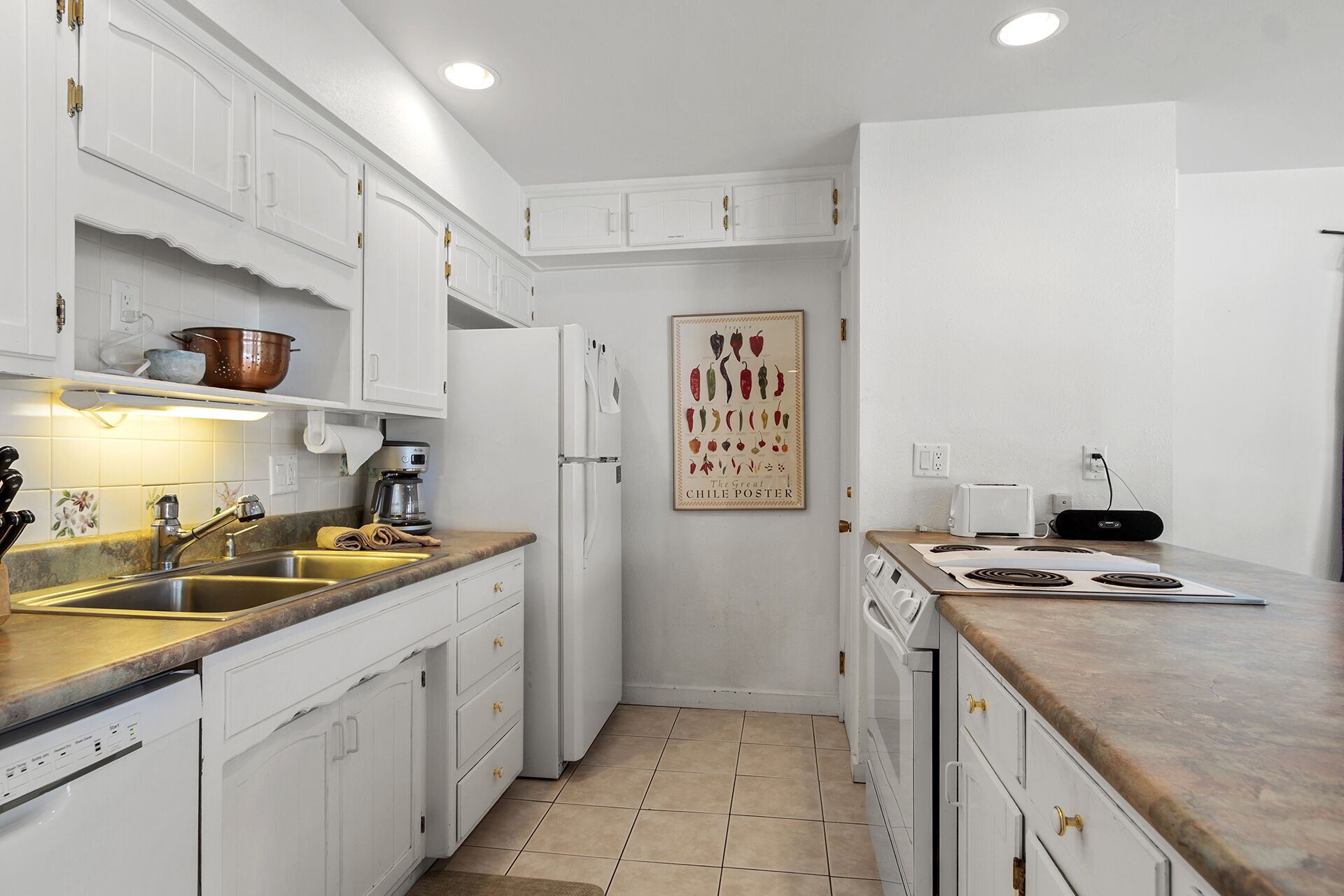 A compact kitchen with white cabinetry, a coffee maker, a toaster, and a poster on the wall.