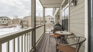 Ein überdachter Balkon mit Tisch und Stühlen, mit Blick auf eine Wohngegend mit Häusern und verschneitem Grund.
