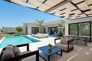 A modern outdoor living space with a pool, lounge chairs, a dining area, and a covered patio. - Trapezia Luxury Living - Opal (Afantou)