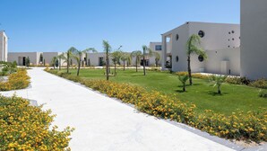 Un ensemble immobilier moderne composé de plusieurs bâtiments, avec un chemin central, le tout entouré de verdure et de palmiers.