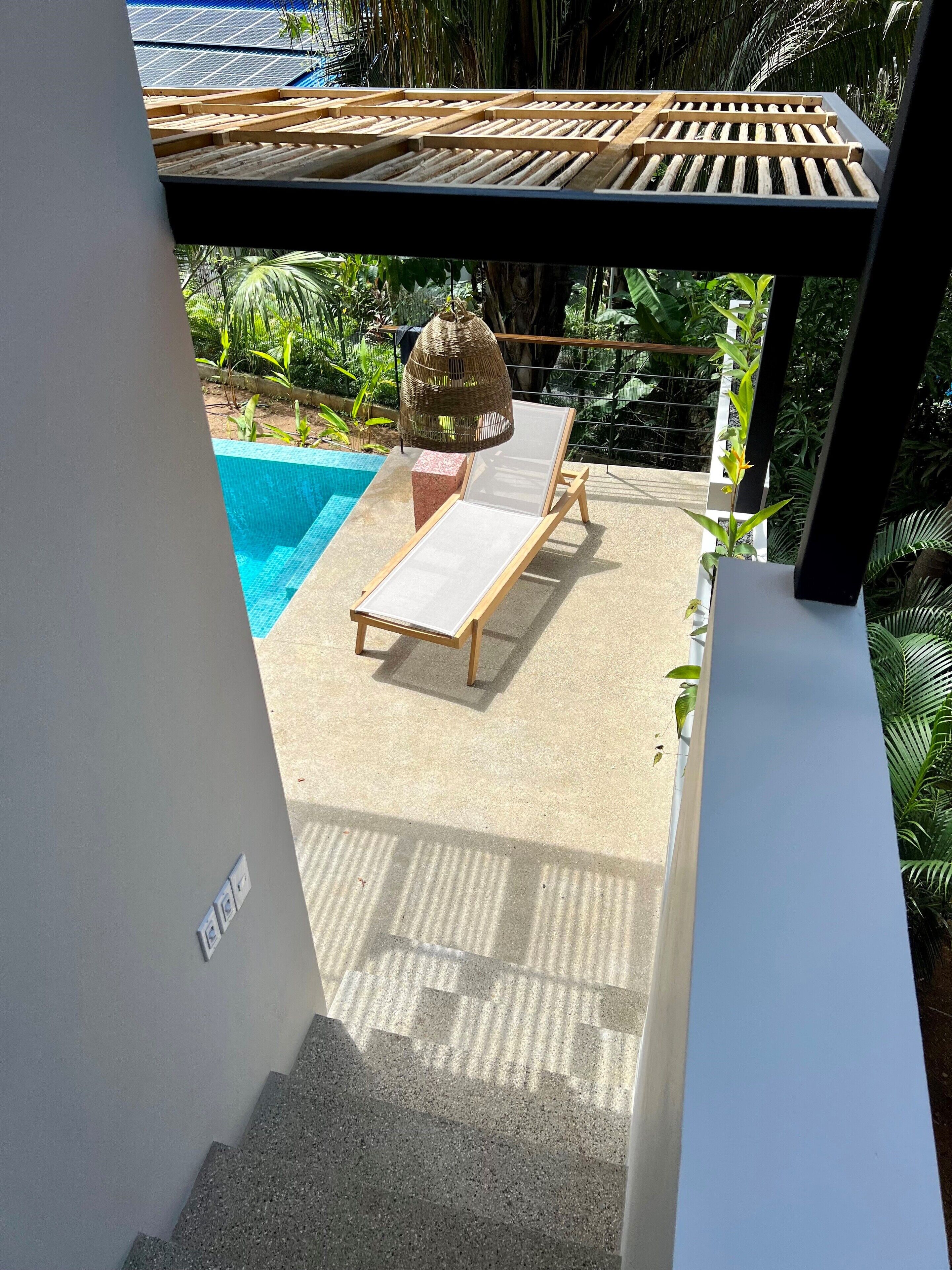 Ein Poolbereich mit Holz-Pergola, einer Liege und einer hängenden Leuchte.