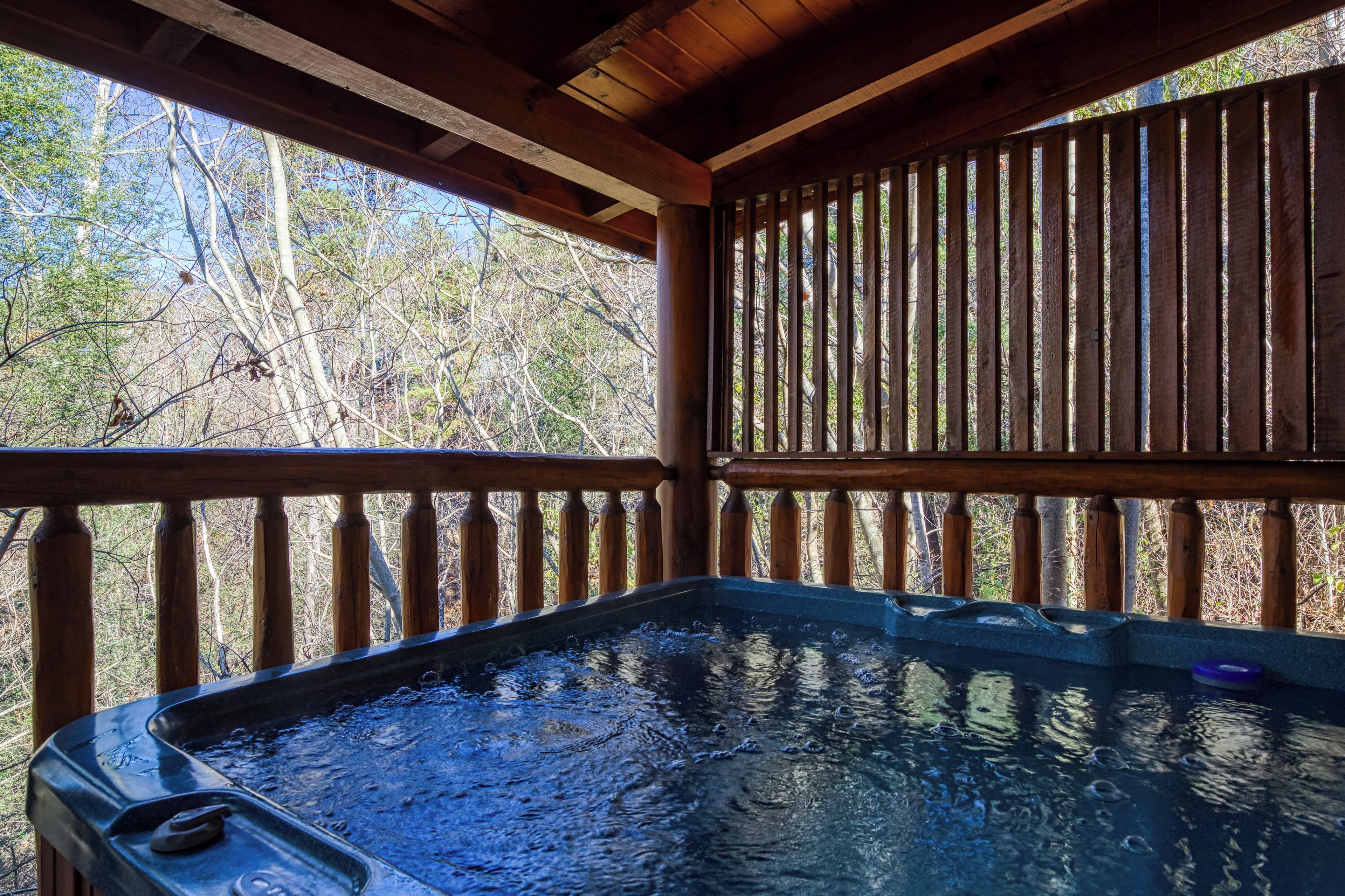A hot tub with a wooden deck and railing, surrounded by trees.