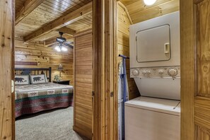 A wooden cabin interior with a bed, a ceiling fan, and a washing machine. - Pigeon Forge | Pool Table | Arcade | Resort Pool | Hot Tub (Sevierville)