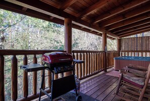 An outdoor deck with a grill, a hot tub, and a wooden chair.