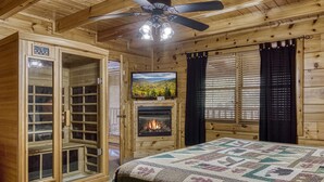 Ein Holzblockhaus-Interieur mit Bett, Kamin, Fernseher und Deckenventilator.