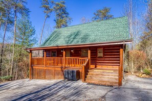 A wooden cabin with a green roof, a porch, and a staircase leading to the entrance.