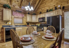 Cocina estilo cabaña de madera con una mesa de comedor preparada para cuatro personas, equipada con refrigerador, estufa y microondas.