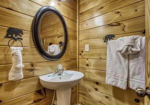 A wooden-paneled bathroom with a white sink, a mirror, and two towels hanging on hooks. - Pigeon Forge | Pool Table | Arcade | Resort Pool | Hot Tub (Sevierville)
