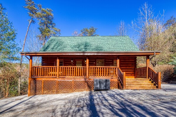 A wooden cabin with a green roof, a wooden porch, and a staircase leading to the entrance.