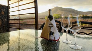 Una mesa con una botella de vino y dos copas, con una vista panorámica de montañas al fondo.