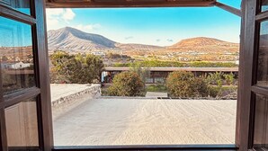 Vista desde una ventana que muestra un paisaje montañoso, una zona pavimentada y algo de vegetación.