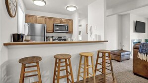 Una cocina moderna con armarios de madera, electrodomésticos de acero inoxidable y una zona de bar con taburetes.