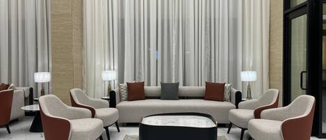 A modern living room with a sectional sofa, armchairs, a coffee table, and a large window with curtains.