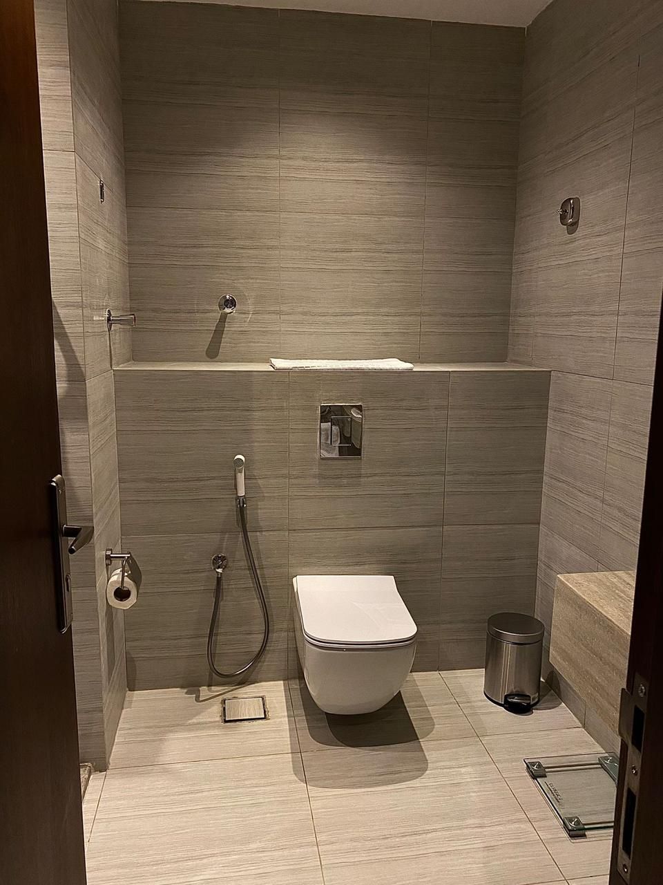 A modern bathroom with a toilet, shower, and a small trash bin.