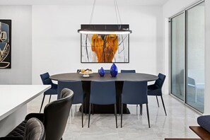 A modern dining area with a round table, blue chairs, and a large abstract painting above. - Casper's Courtyard | Fab home w science lab themed room, PVT pool - near airport (Orlando)
