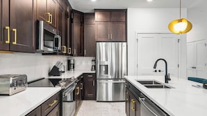 Una cocina moderna con armarios de madera oscura, electrodomésticos de acero inoxidable y encimera blanca.