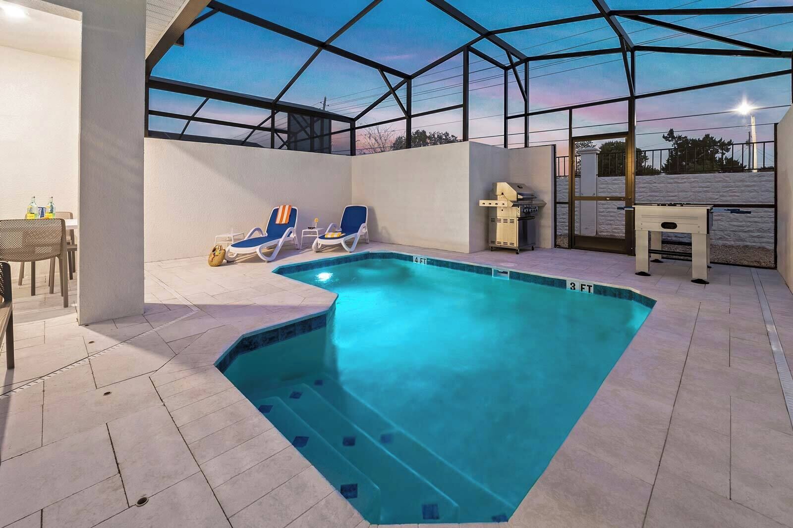 Una piscina con sillones de descanso y zona de barbacoa, rodeada por un porche cubierto.