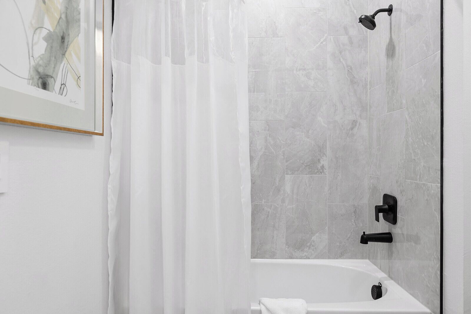 Een moderne badkamer met een bad, een douche met een handdouche en een wandmengkraan.