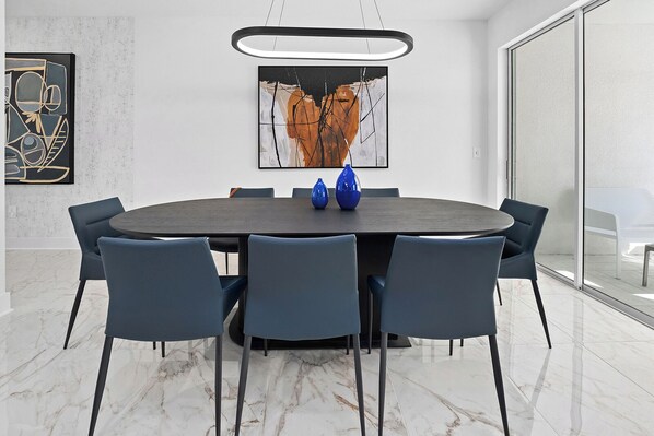 A modern dining area with a round table, six chairs, and two blue vases.