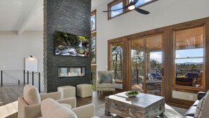 A modern living room with a stone fireplace, comfortable seating, and large windows offering a view of the outdoors.