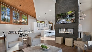 A spacious living area with a fireplace, modern furniture, and a view of the kitchen.