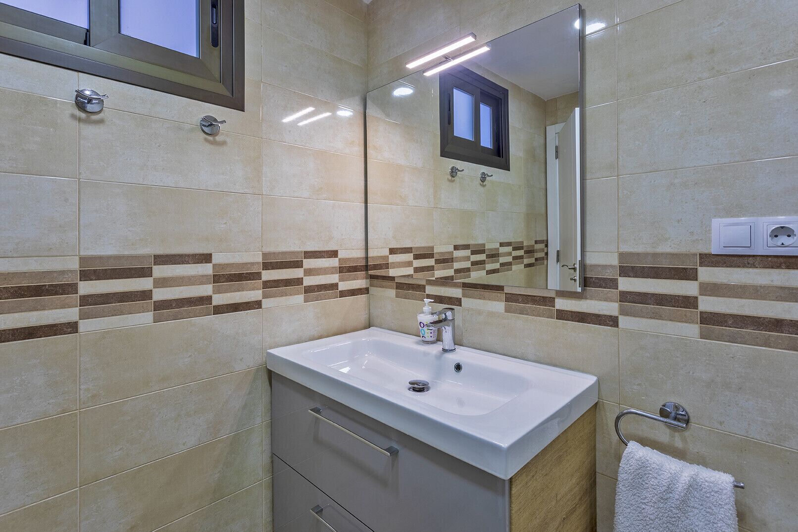 Un baño con un lavamanos blanco, un espejo y un perchero para toallas.
