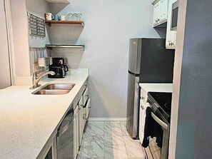 A compact kitchen with a sink, a coffee maker, a refrigerator, and cabinets.
