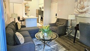 A living room with a sofa, armchair, coffee table, and a painting on the wall. - I30 - Apt|Patio|11mi to Convention Ctr|Sleeps 2 (Irving)
