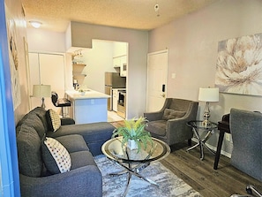 A living room with a sofa, armchair, coffee table, and a painting on the wall. - I30 - Apt|Patio|11mi to Convention Ctr|Sleeps 2 (Irving)