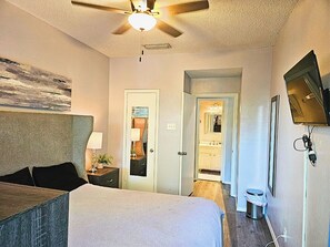 A bedroom with a bed, a ceiling fan, a nightstand, a mirror, and a television mounted on the wall.