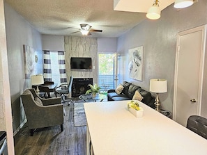 A modern living room with a fireplace, a ceiling fan, and a flat-screen TV mounted on the wall.