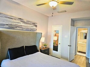 A bedroom with a bed, a nightstand, a ceiling fan, a door, and a view of a bathroom. - I30 - Apt|Patio|11mi to Convention Ctr|Sleeps 2 (Irving)
