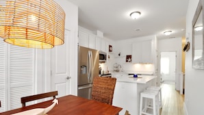 A modern kitchen with white cabinets, a stainless steel refrigerator, and a microwave. There is a dining area with a wooden table and chairs. - "Dock, Relax, and Unwind at Waterside Retreat!" (Mexico Beach)