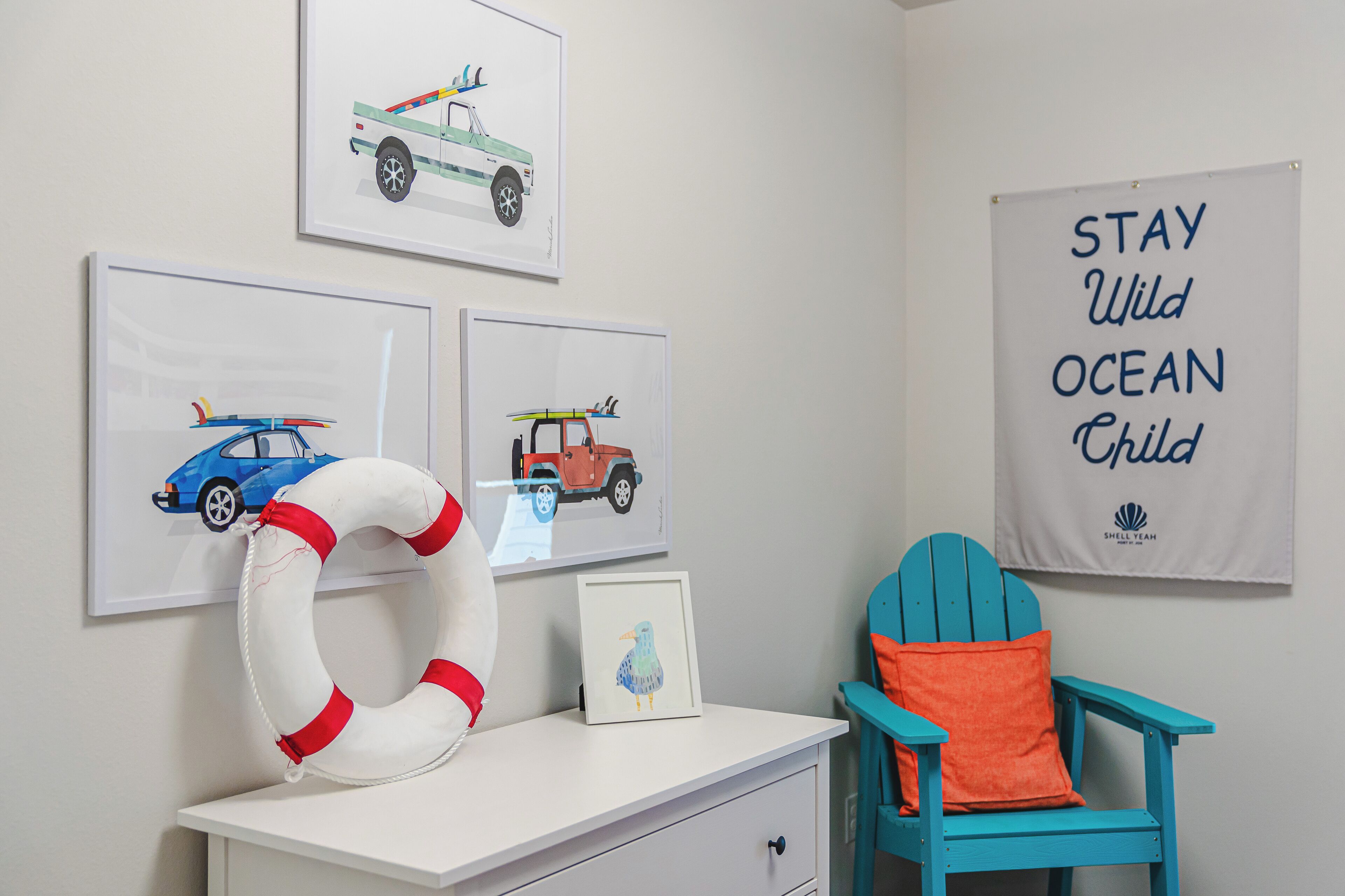 A room with a white desk, a blue chair, and artwork on the wall.