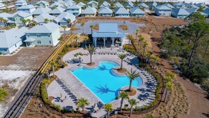 Vue aérienne d’un complexe hôtelier doté d’une piscine centrale, entourée d’espaces de détente et de palmiers.