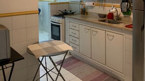 Une cuisine de taille réduite, avec des meubles blancs, une cuisinière à gaz, un évier et un réfrigérateur.