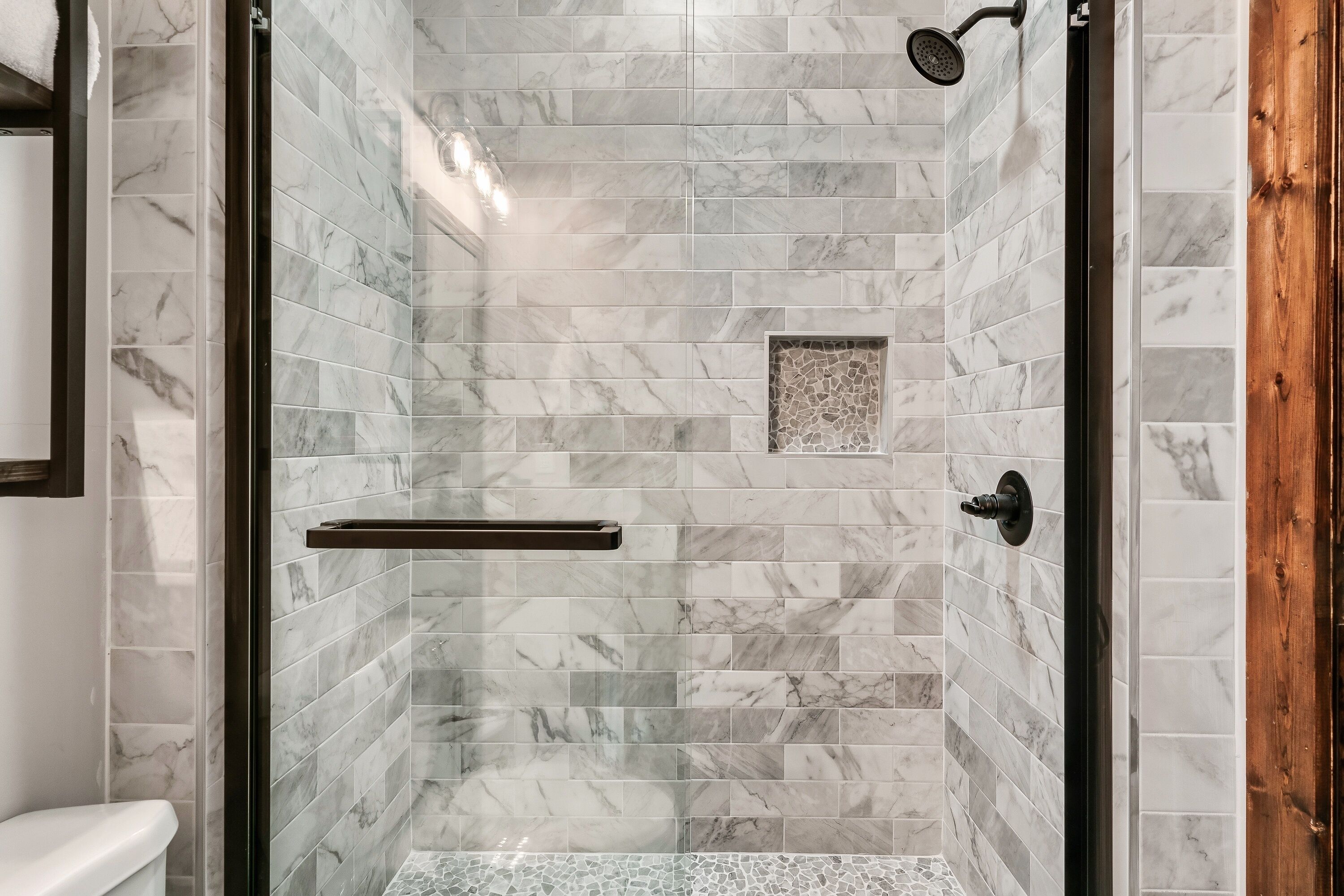 A shower with a glass door, marble tiles, and a wooden door frame.