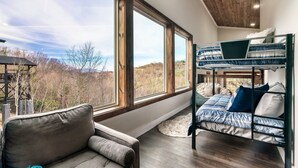 A bedroom with a bunk bed, a sofa, and large windows offering a view of the outdoors. - Fall Getaway! Hot Tub! Mountain Views! (Gatlinburg)