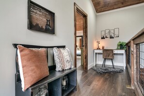 Een moderne woonkamer met een zwarte bank, decoratieve kussens, een houten bankje en een bureau met een plant.