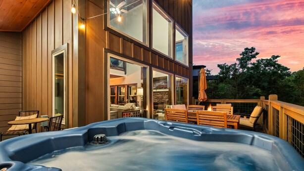 A hot tub on a wooden deck with a view of a modern house and a sunset. - Fall Getaway! Hot Tub! Mountain Views! (Gatlinburg)